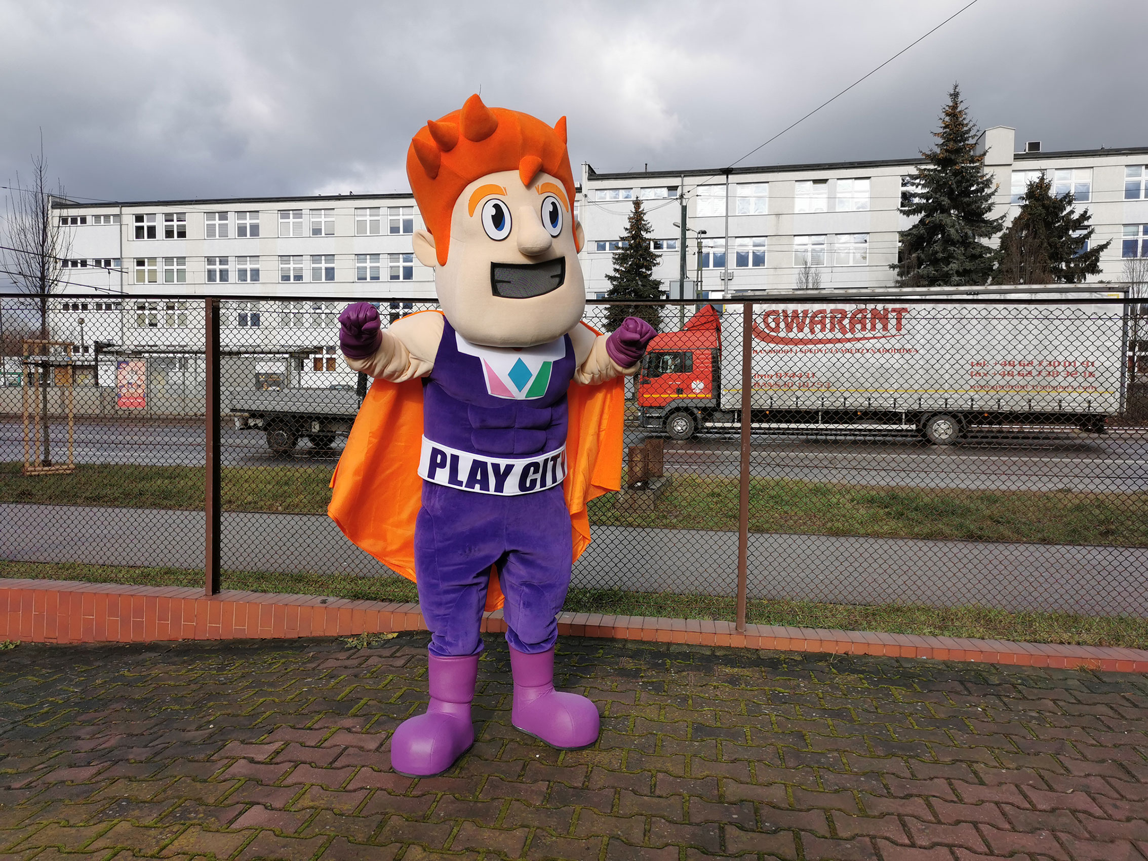Na fotografii widnieje przebranie za chłopaka superbohatera pozujące do zdjęcia przed siedzibą firmy Elabika